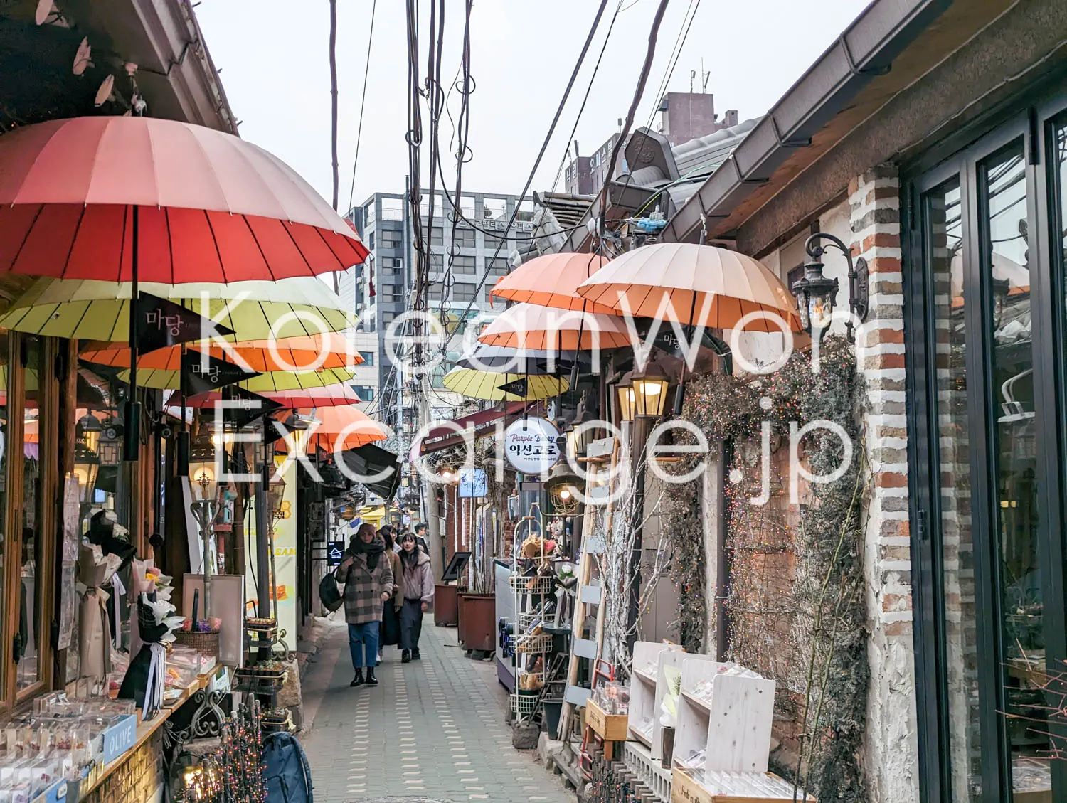 A narrow Seoul alley. Colorful umbrellas hang overhead between vintage shops and crafts stores.